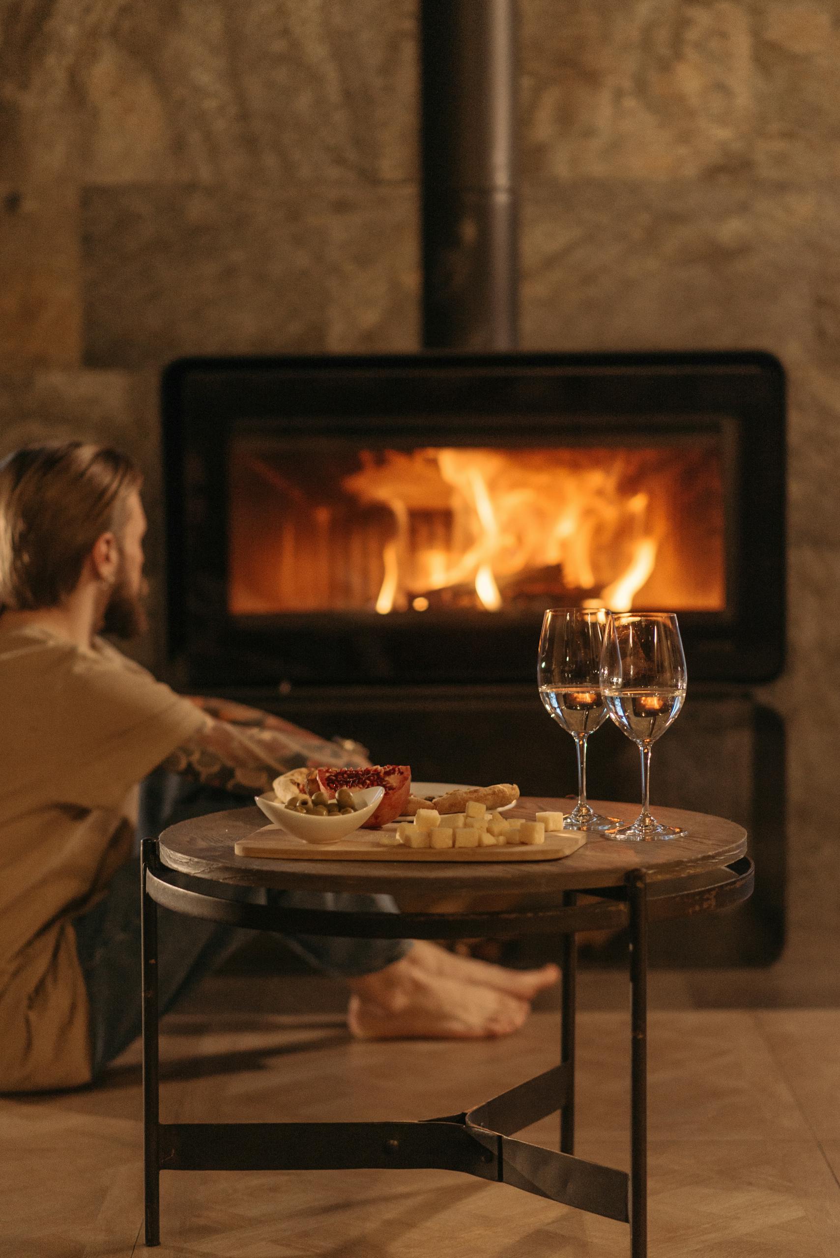 A warm, inviting scene of a person relaxing by a fireplace with cheese and wine.